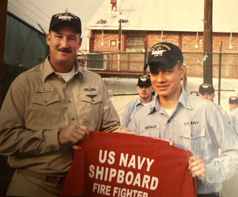 Juan Gonzalez (right) as a young sailor during his U.S. Navy service, holding a US Navy Shipboard Fire Fighter banner
